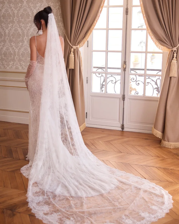 Voile cathédrale de dentelle, de dos, devant les portes-fenêtres d’un salon